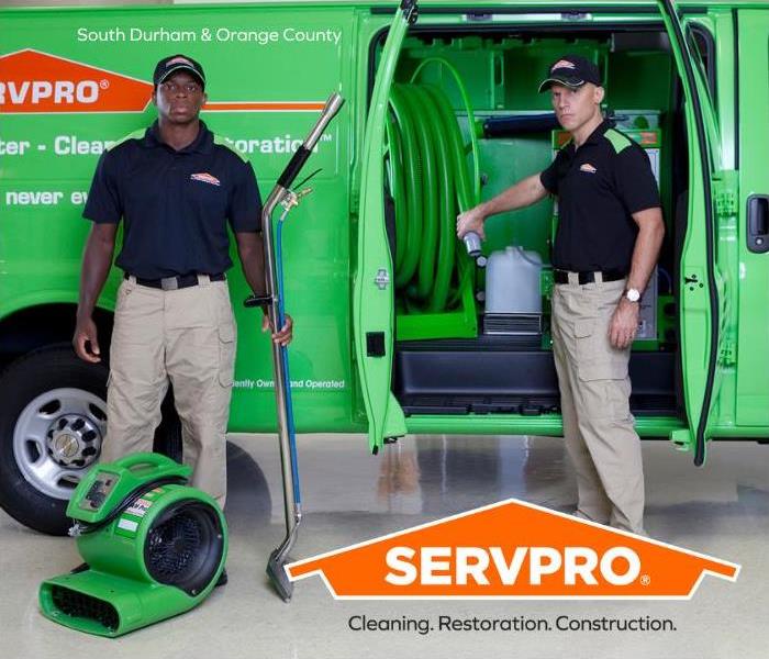 2 employees in front of a green Servpro van with equipment 